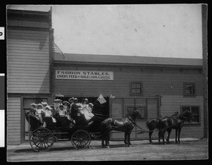 Horse-drawn carriage filled with children in front of a livery stable, 1906