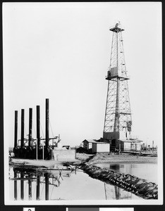 Unidentified oil well, showing a body of water in the foreground, ca.1930