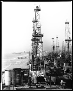 View of an H.R. Dabney oil field on Playa del Rey in Venice, with a paved street running between the oil derricks, ca.1925