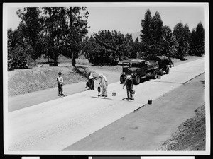 Four men using tar to fill in the cracks in concrete sections of street