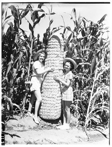 Two young women standing next to a giant ear of corn, Pomona County Fair, 1936