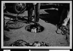 Department of Public Works employee entering a gas-filled manhole wearing a gas mask