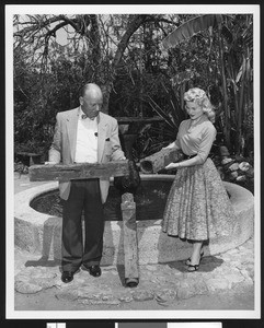 Two unidentified people holding hallowed logs from the first pipes used for domestic water, ca.1950