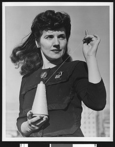 Portrait of a female garment worker holding a spool of thread in a pose for the camera, ca.1940