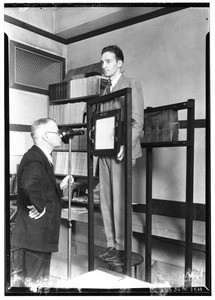 Doctor using what appears to be part of an early model X-ray machine on a male patient