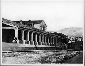 Exterior view of Mission San Luis Obispo de Tolosa, showing the arcade in front of the south wing, ca.1875
