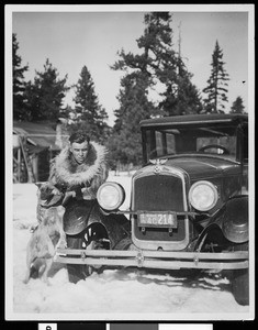 Man in a fur coat and dog next to automobile in snow, ca.1926