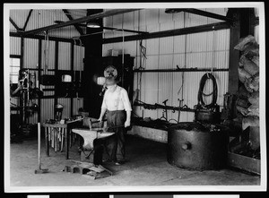 Department of Public Works worker hammering metal inside a smithy