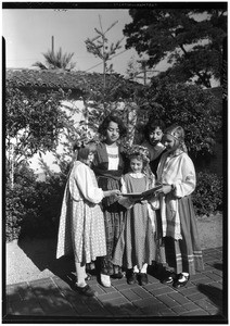 Five girls standing outside a home looking at an open book, 1933