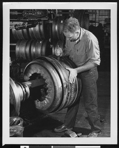 Factory worker applying a tool to a tire, ca.1930