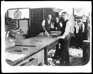 Three men gathered around a table at Tom Williams' tailor shop on Main Street in Los Angeles, ca.1880-1889