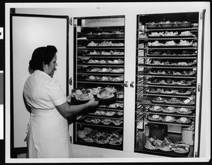 Cafeteria worker handing food at the door of a refrigerator in the kitchen of an unknown school