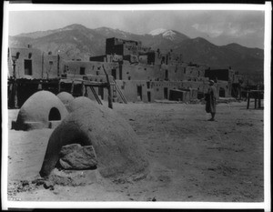 Man standing in front of an Indian pueblo in Taos, New Mexico, 1932