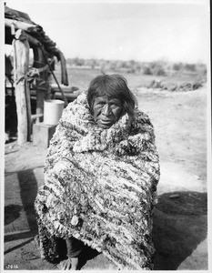 Mojave Indian woman sitting outside wrapped in a rabbit-skin blanket, ca.1900