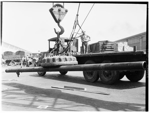 Steel pipe being loaded onto a flatbed truck via a large magnet at Los Angeles Harbor, 1930