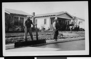 Two workers spraying asphalt along the curb of York Boulevard as part of the Hunt curing process