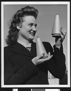 Portrait of a female garment worker holding two spools of thread in a pose for the camera, ca.1940