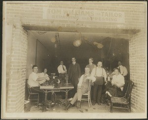 Interior view of Tom Williams' tailor shop, showing men and women working in room, ca.1880-1889