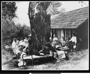 People camping out on cots in front of a house, ca.1920