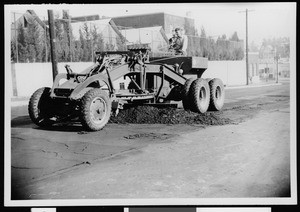 Man using a specialized tractor to scrape off the old surface of a street marked for resurfacing