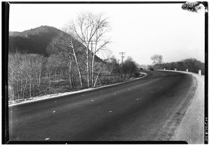 Unidentified curved road running past a hillside, with light traffic running down the right side