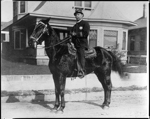 Portrait of a mounted Los Angeles policeman in front of a residence, ca.1900-1909