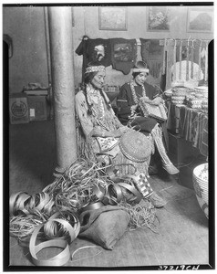 Two Native American women weaving baskets indoors