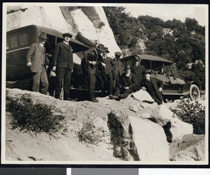 Men around early automobiles looking over a cliff