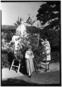 Four girls tying ornaments on a small Christmas tree outside a home