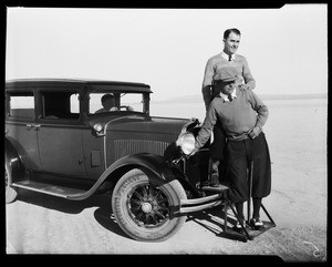 Two golfers standing on the front bumper of an automobile