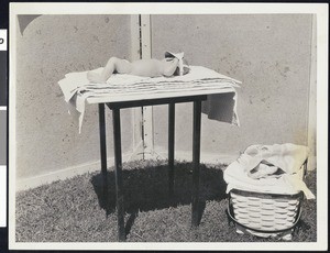 A baby lying in the sun while wearing a visor, ca.1920-1930