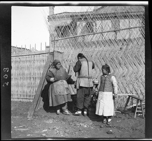 Man, woman and child working on a thatch wall in China, ca.1900