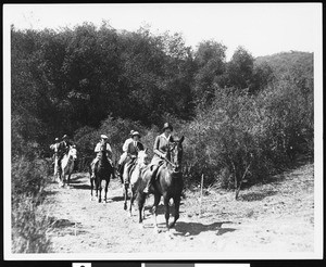 A group of men and women horseback riding along a dirt road, ca.1930