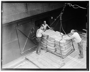 Three workers loading or unloading packages of raw silk onto a ship