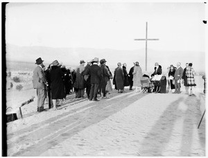 Group of people gathered near a cross for a funeral in the desert