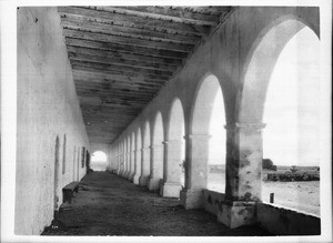 Exterior of Mission San Fernando Rey de Espana, looking east through corridor showing fountain, ca.1900