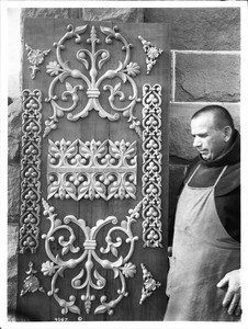 Franciscan monk standing by an intricately decorated wooden panel at Mission Santa Barbara, California, ca.1901-1908