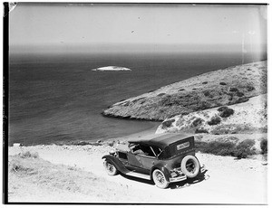 Early-model automobile on a hill overlooking the ocean