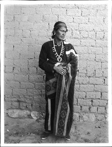 Navajo chieftain standing outside in front of an adobe wall, Tohatchi, New Mexico, ca.1900