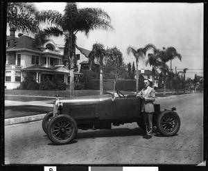 Man in a suit standing next to an open-air automobile, ca.1920