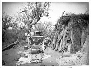 Apache Indian woman basket maker in front of her dwelling, ca.1900