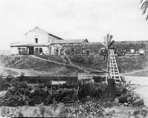 Exterior view of Mission San Diego Alcala showing a well (or water tank?) in the garden, San Diego, ca.1874