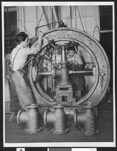 Two men working at a machine inside an unidentified factory, ca.1942