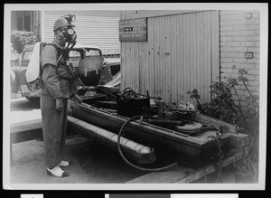 Exterior view of a sewer maintenance yard, showing a Department of Public Works worker wearing a protective mask, ca.1936