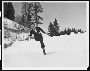 A figure ice skater, wearing an Olympic games insignia, possibly at an ice rink at Big Pines mountain camp, ca.1930