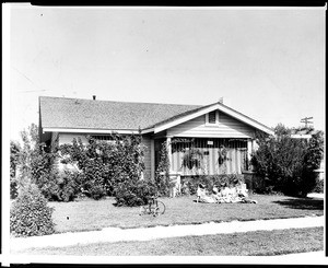 Children sitting in front of a small bungalow typical of those found in California, ca.1928