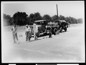 Four men using tar to fill in seams on a nearly completed street