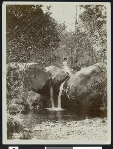 Woman seated on a rock above a small waterfall in Ventura, 1910