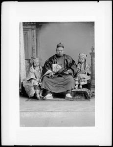 Seated adult Mandarin (father?) flanked by two female children in ceremonial clothes, ca.1880