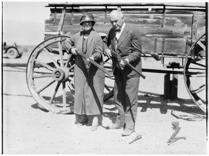 Man and woman holding guns in front of a wagon